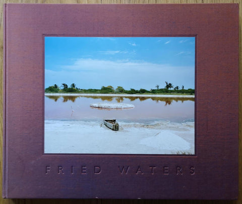 The photography book cover of Fried Waters by Eduardo del Valle and Mirta Gomez. Hardback with a cover image of a boat by a river.