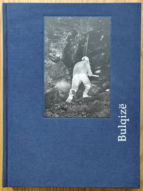 The photography book cover of BULQIZE by Elton Gllava. Hardback in blue with B&W image of a man in a cave.