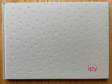 The photography book cover of IPY by Emi Anrakuji. Hardback in light grey with dots all over the cover, IPY in red. Signed.