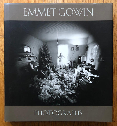 The photography book cover of Emmet Gowin: Photographs by Emmet Gowin. Hardback with image of a woman standing in a room full of opened christmas presents.