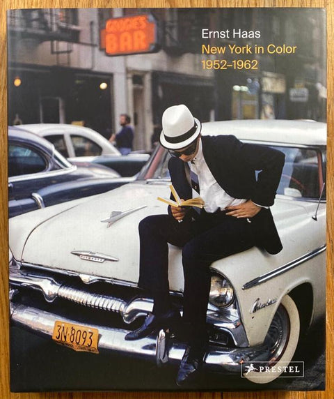 The photography book cover of New York in Color 1952 - 1962 by Ernst Haas. Hardback with image of a man sat on a white car reading a book.
