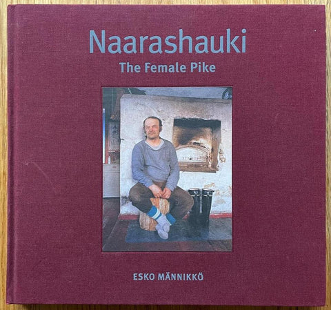The photography book cover of Naarashauki: The Female Pike by Esko Mannikko. Hardback in burgundy with light blue title and image of a man sat on a stool. Signed.