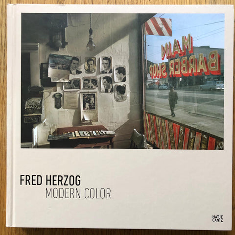 The photography book cover of Modern Color by Fred Herzog. Hardback in white with image of a barbers shop.