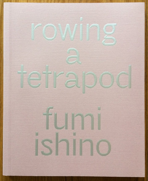 The photography book cover of Rowing in a Tetrapod by Fumi Ishino. Hardback pink cover with silver text.