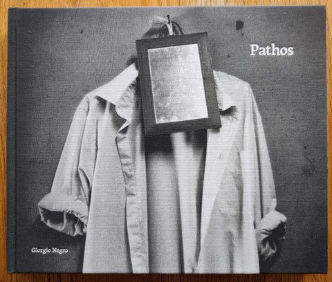 The photography book cover of Pathos by Giorgio Negro. In hardcover black and white with a shirt and a small mirror in a fram hung on a wall.