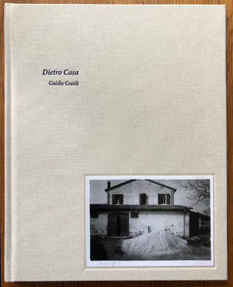 The photography book cover of Dietro Casa by Guido Guidi. Hardback beige with B&W image of house in the bottom corner.