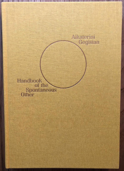 The photography book cover of Handbook of the Spontaneous Other by Aikaterini Gegisian. Hardback in yellow with a circle in the centre. Signed.