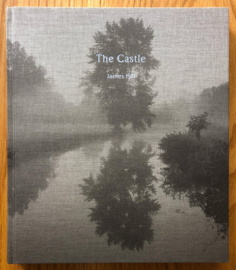 The photography book cover of The Castle by James Hill. Hardback in B&W image of trees reflection in lake.