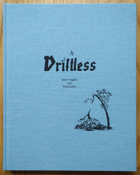 The photography book cover of Driftless by Jason Vaughn and Brad Zellar. Hardback in blue with small drawing of a broken tree on the cover.