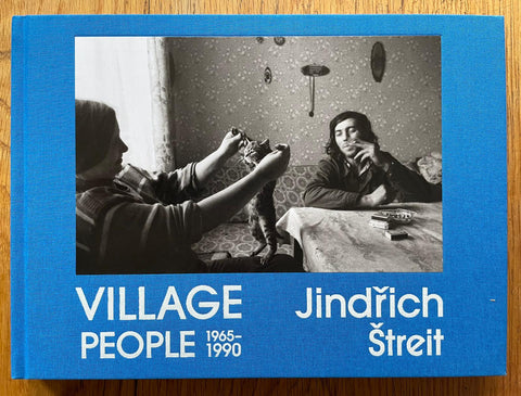The photography book cover of Village People 1965 - 1990 by Jindrich Streit. Hardback in light blue with image of a woman playing with a cat.