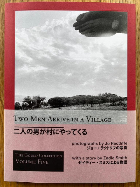 The photography book cover of Two Men Arrive in a Village (The Gould Collection Volume Five) by Jo Ractliffe and Zadie Smith. Paperback in red.