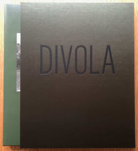 The photography book cover of San Fernando Valley by John Divola. Hardback case in black with "DIVOLA" in the middle, encasing a hardback green book cover.