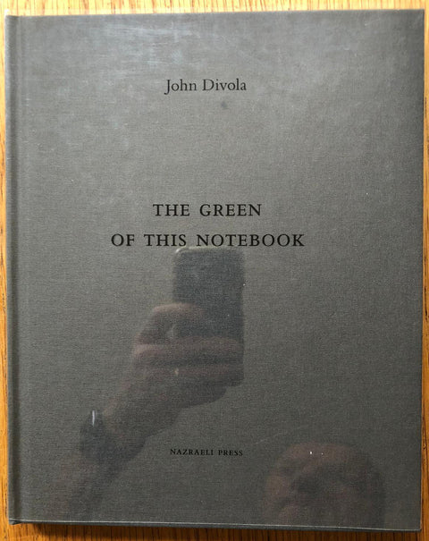 The photography book cover of The Green of this Notebook by John Divola. Hardback in dark grey with glassine jacket.