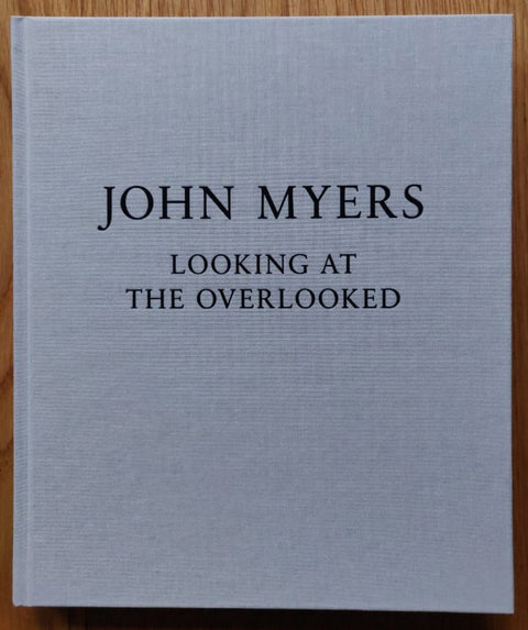 The photography book cover of Looking at the Overlooked by John Myers. Hardback in white with black text.