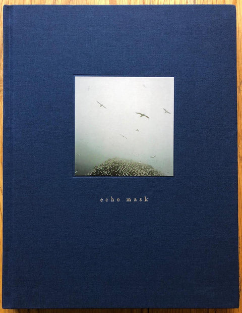 The photography book cover of Echo Mask by Jonathan Levitt. Hardback in dark blue with image of birds flying through fog.