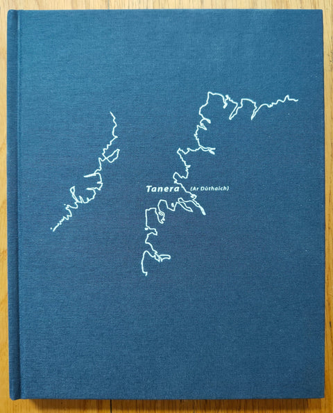 The photography book cover of Tanera (Ar Duthaich) by Kevin Percival. Hardback in blue with white coast outline.