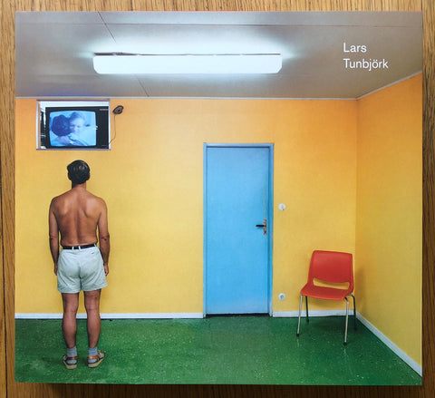 The photography book cover of Lars Tunbjork: Retrospective. Hardback with image of a topless man standing in a room with yellow walls.