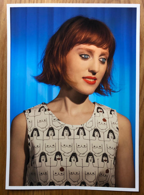 The photography book cover of How We See by Laurie Simmons. Hardback in blue with print of a red haired doll girl on the cover.
