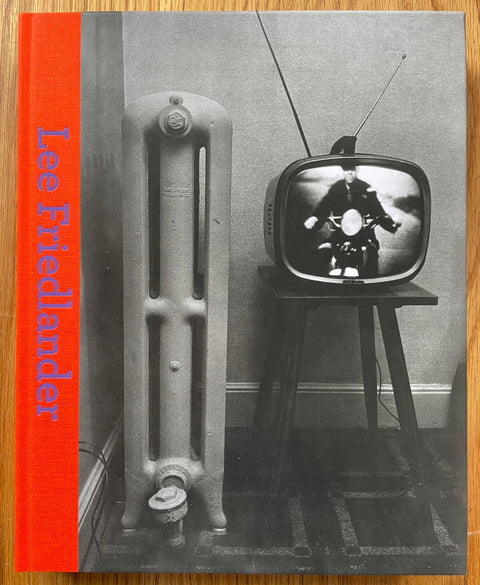 The photography book cover of Lee Friedlander by Lee Friedlander. Hardback in B&W with orange binding and purple title.
