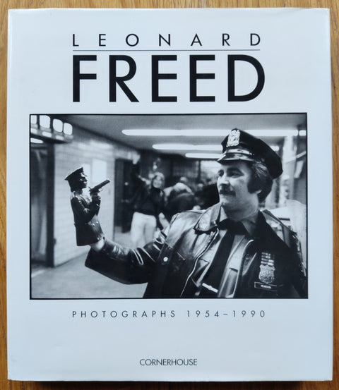 The photography book cover of Photographs 1954 - 1990 by Leonard Freed. Hardback in white with image of a policeman.