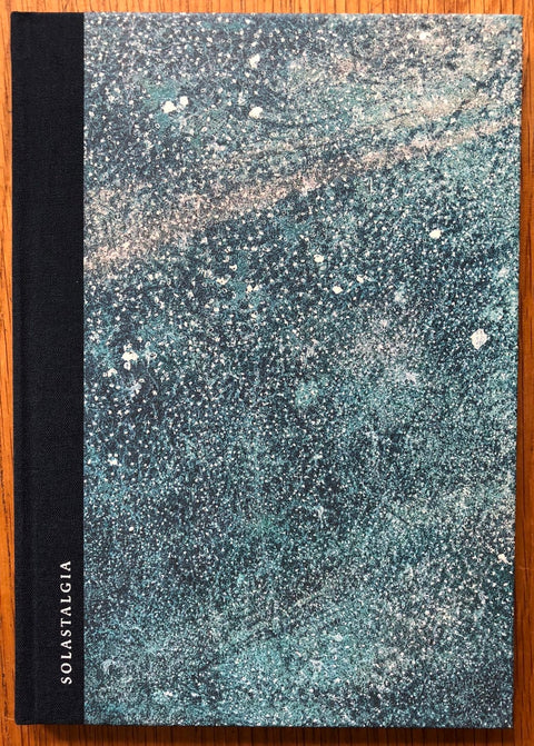 The photography book cover of Solastalgia by Marina Vitaglione. Hardback with a blue, white and black speckled cover.