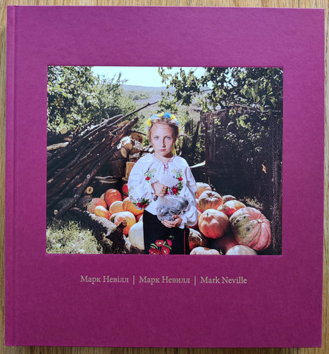 The photography book cover of Stop Tanks With Books by Mark Neville. In hardcover red with a photo of Lina in a national costume. 