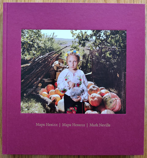 The photography book cover of Stop Tanks With Books by Mark Neville. In hardcover red with a photo of Lina in a national costume. 