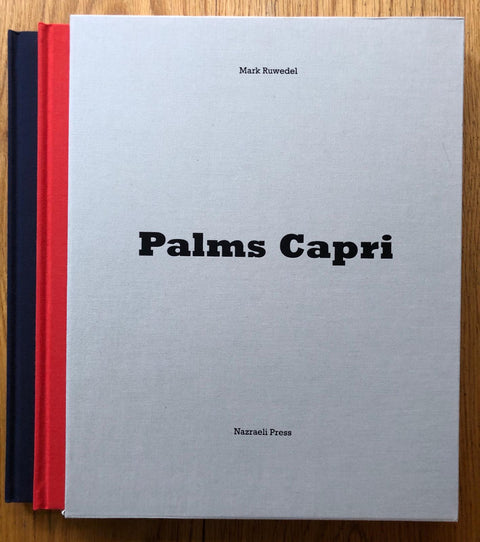 The photography book cover of Palms Capri by Mark Ruwedel. Hardback in red and navy blue with white slipcased cover.