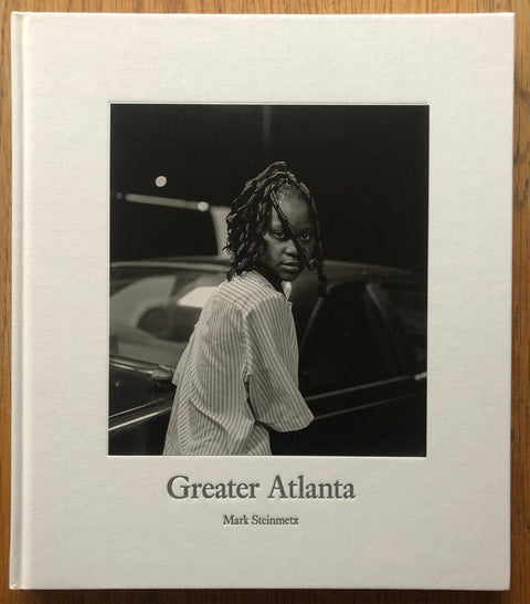 The photography book cover of Greater Atlanta by Mark Steinmetz. Hardback in white with image of a child in striped white top looking into the camera.