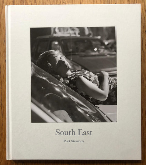 The photography book cover of South East by Mark Steinmetz. Hardback with B&W image of a woman lying on her car. Signed.