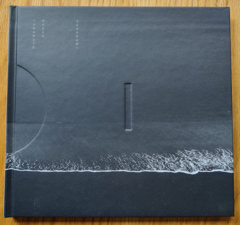 The photography book cover of Sasanami by Masao Yamamoto. Hardback in black with a wave breaking at shore. Numbered and stamped.