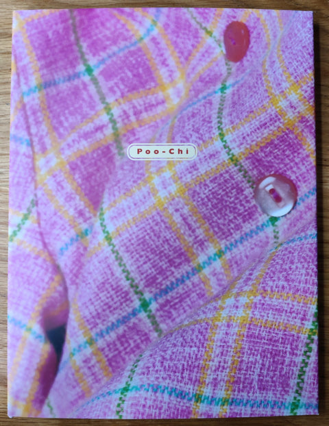 The photography book cover of Poo-Chi by Mayumi Lake. Hardback with image of pink blue yellow and green checked clothing with buttons.