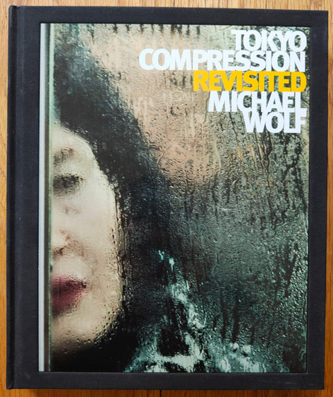 The photography book cover of Tokyo Compression Revisited by Michael Wolf. Hardback in black with white title and yellow "revisited".