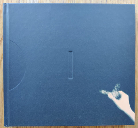 The photography book cover of Flowers Bloom, Butterflies Come by Miho Kajioka. Hardback in navy blue with image of a hand holding onto a butterfly.