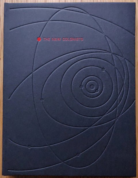 The photography book cover of The New Colonists by Monica Alcazar Duarte. Hardback in dark navy with indented curved lines. Red title.