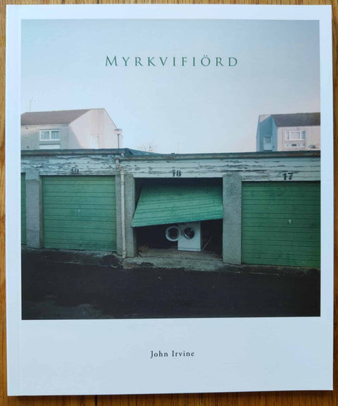 The photography book cover of Myrkvifiord by John Irvine. Paperback photograph of an open green-doored storage unit with a washing machine inside.