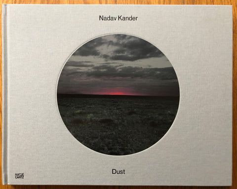 The photography book cover of Dust by Nadav Kander. Hardback grey cover with image of a dark sky in a circle in the middle.
