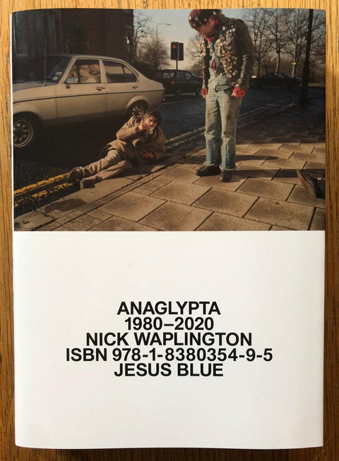 The photography book cover of Anaglypta 1980 - 2020 by Nick Waplington. Paperback with image of a man lying on a double yellow line.