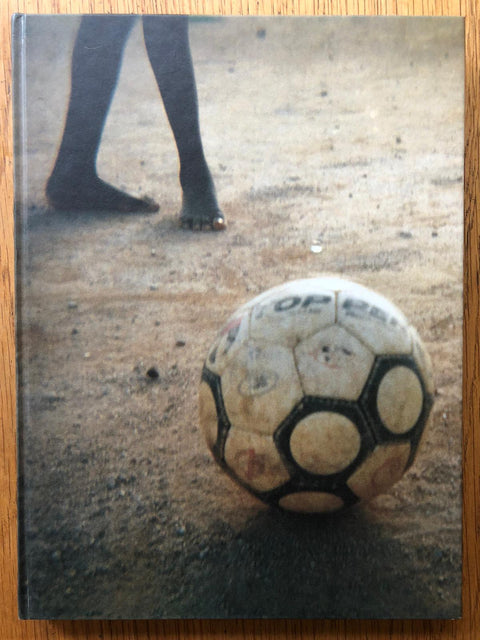 The photography book cover of No Mundo Maravilhoso do Futebol by Julian Germain, Murilo Godoy and Patricia Azevedo. Hardback cover image of football.