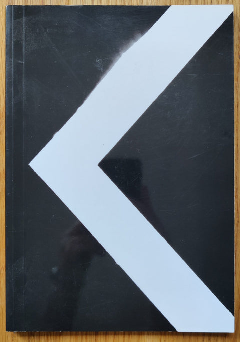 The photography book cover of KARMA by Oscar Monzon. Paperback in black with a white arrow on the cover.