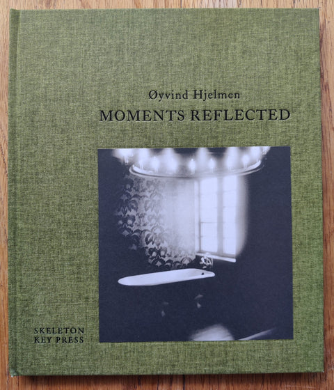 The photography book cover of Moments Reflected by Oyvind Hjelman. Hardback in green with  picture of a bath. Signed.
