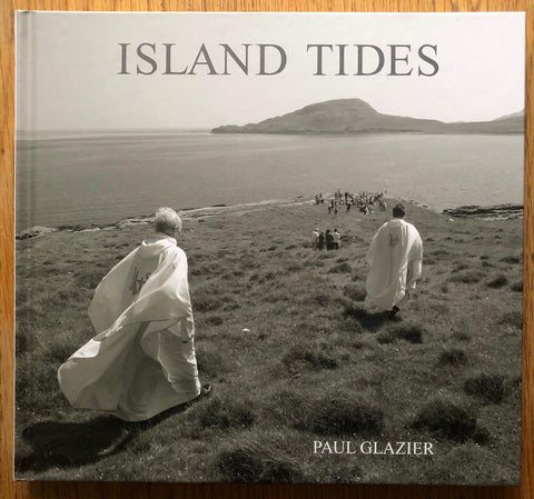 The photography book cover of Island Tides by Paul Glazier. Hardback with image of people walking towards the sea in long white outfits.