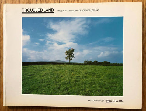 The photography book cover of Troubled Land by Paul Graham. Paperback with photograph of a tree from a field.
