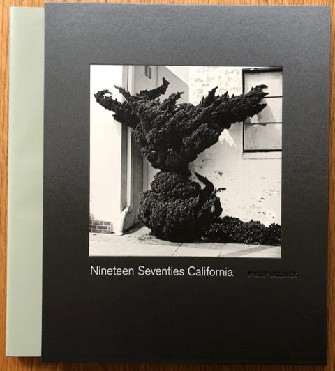 The photography book cover of Nineteen Seventies California by Philip Melnick. Hardback in black with cover image of a weirdly shaped bush outside a house.
