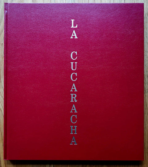 The photobook cover of La Cucaracha by Pieter Hugo. Hardback in red with silver title printed vertically down the middle. Signed.
