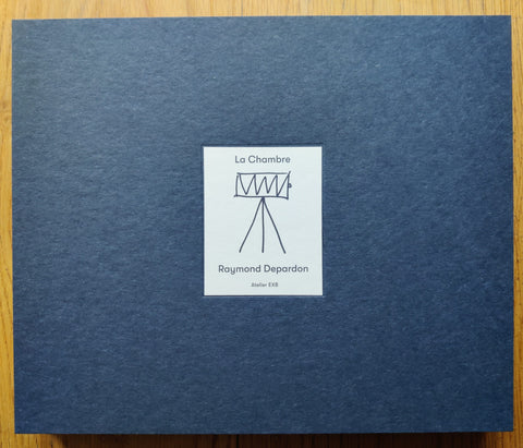 The photography book cover of La Chambre by Raymond Depardon. Hardback in navy blue with drawing of a camera on a tripod.
