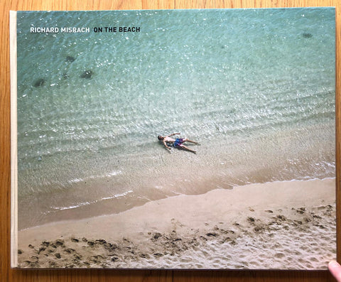 The photography book cover of On The Beach by Richard Misrach. Hardback with image of a man lying in the sea on the beach.