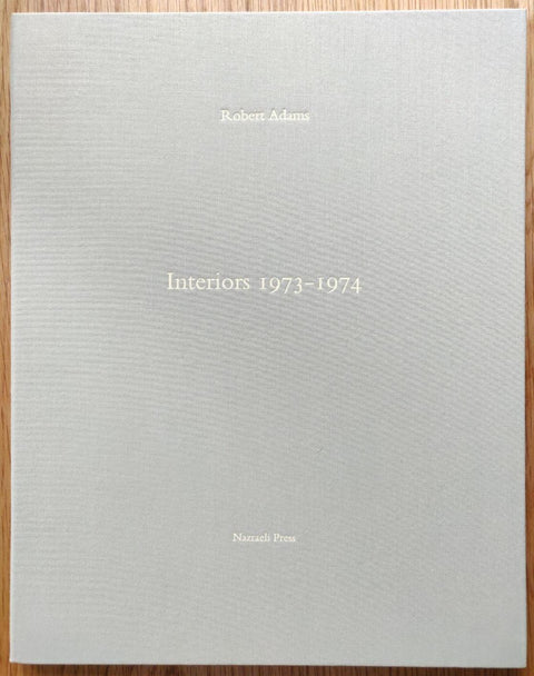 The photography book cover of Interiors 1973-1974 by Robert Adams. In hardcover grey.
