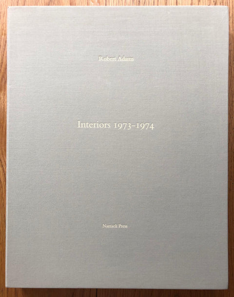 The photography book cover of Interiors 1973-1974 by Robert Adams. Hardback in light grey. Signed.