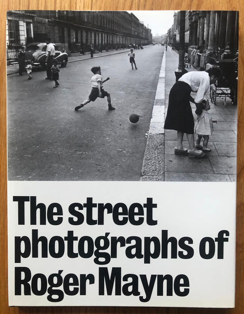 The photography book cover of The Street Photographs of Roger Mayne by Roger Mayne. Paperback with image of a boy running by a ball in the road.